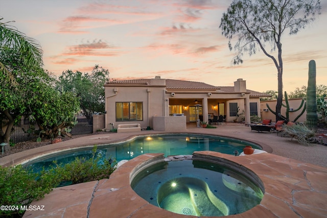 pool at dusk with a patio and an in ground hot tub