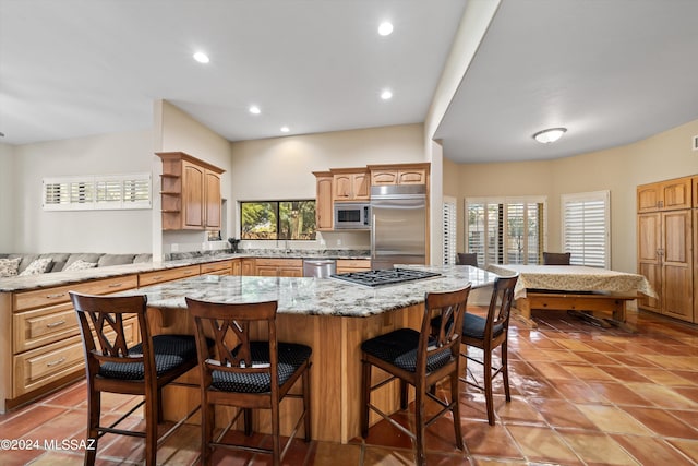 kitchen with a breakfast bar, light stone counters, built in appliances, a kitchen island, and tile patterned floors