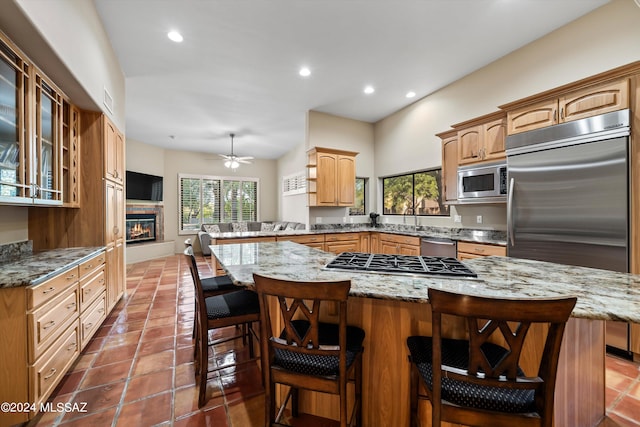 kitchen featuring light stone counters, kitchen peninsula, built in appliances, a kitchen bar, and ceiling fan