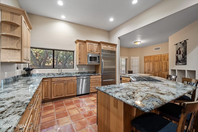 kitchen with sink, built in appliances, a center island, a breakfast bar area, and light stone countertops