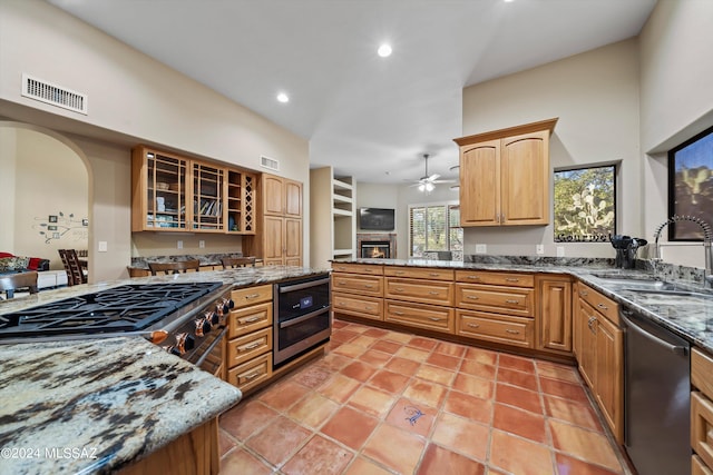 kitchen with stone countertops, light tile patterned floors, stainless steel appliances, ceiling fan, and sink