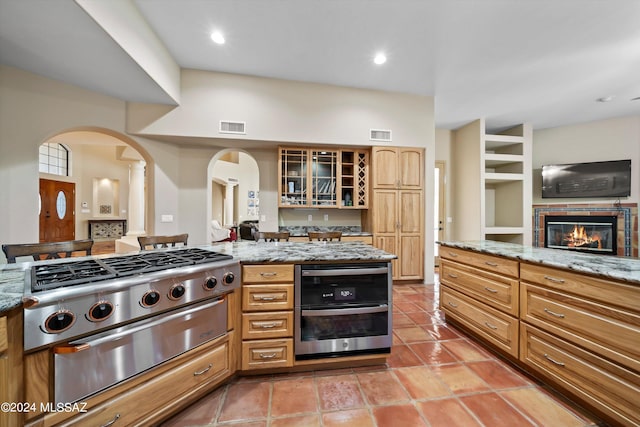 kitchen featuring light stone counters, stainless steel double oven, a tiled fireplace, and light tile patterned floors