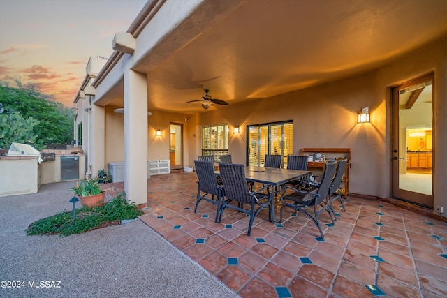 patio terrace at dusk with area for grilling, ceiling fan, and a grill