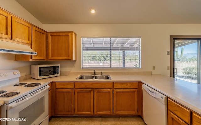 kitchen with brown cabinets, a sink, under cabinet range hood, white appliances, and light countertops