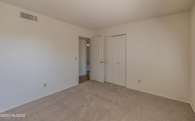 unfurnished bedroom featuring baseboards, light colored carpet, visible vents, and a textured ceiling