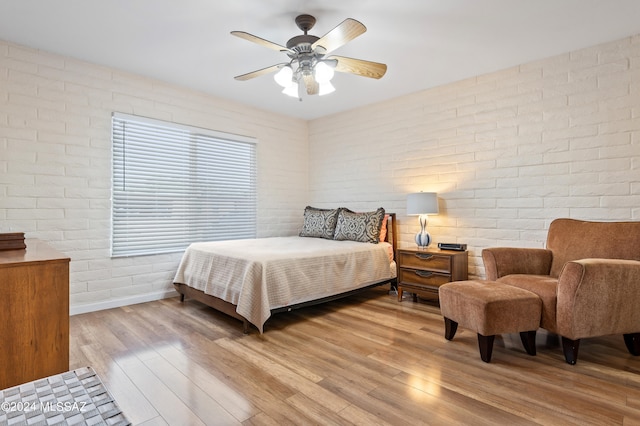 bedroom featuring light hardwood / wood-style flooring, ceiling fan, and brick wall