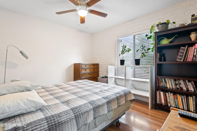 bedroom featuring wood-type flooring, ceiling fan, and brick wall