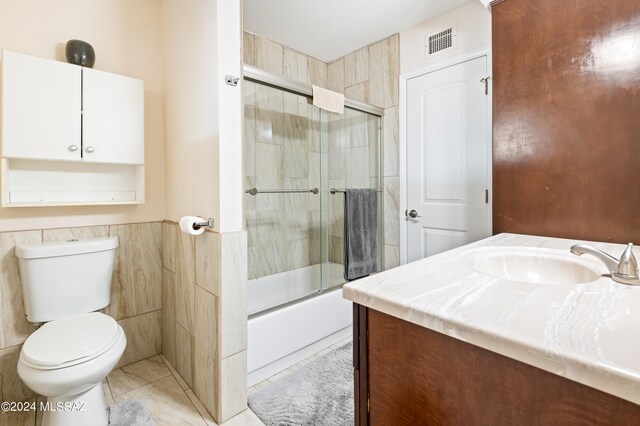 full bathroom featuring tile walls, enclosed tub / shower combo, vanity, and toilet