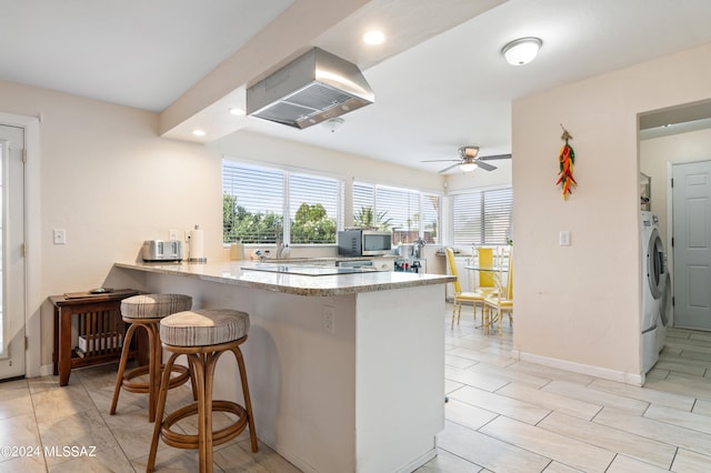 kitchen with washer / dryer, a breakfast bar area, kitchen peninsula, island range hood, and ceiling fan