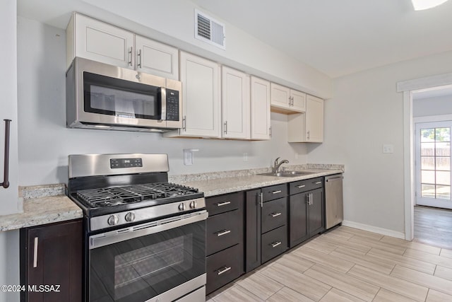 kitchen with white cabinets, sink, dark brown cabinets, light stone counters, and stainless steel appliances