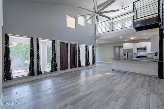 unfurnished living room featuring a towering ceiling, light hardwood / wood-style floors, and ceiling fan