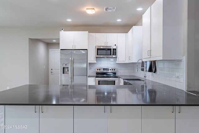 kitchen featuring backsplash, a kitchen breakfast bar, kitchen peninsula, appliances with stainless steel finishes, and white cabinetry