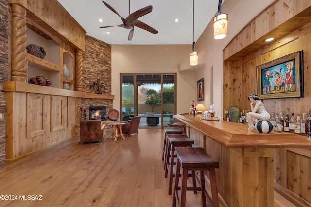 bar with a stone fireplace, hanging light fixtures, built in features, wood walls, and light hardwood / wood-style flooring