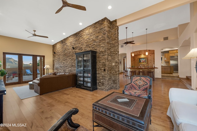 living room with ceiling fan, a towering ceiling, hardwood / wood-style flooring, and french doors