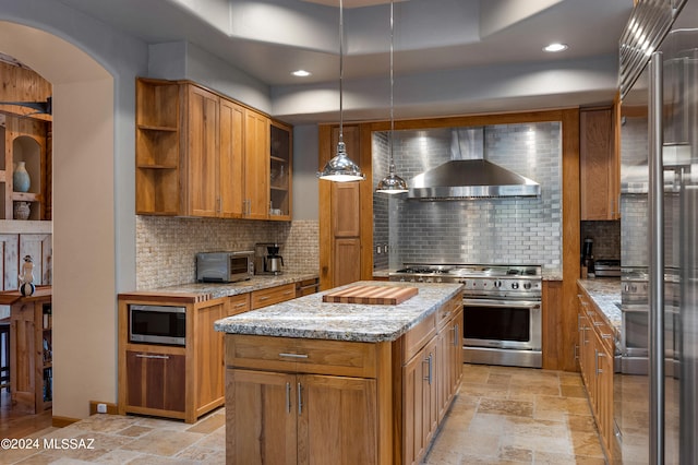 kitchen with premium appliances, tasteful backsplash, hanging light fixtures, wall chimney range hood, and a center island