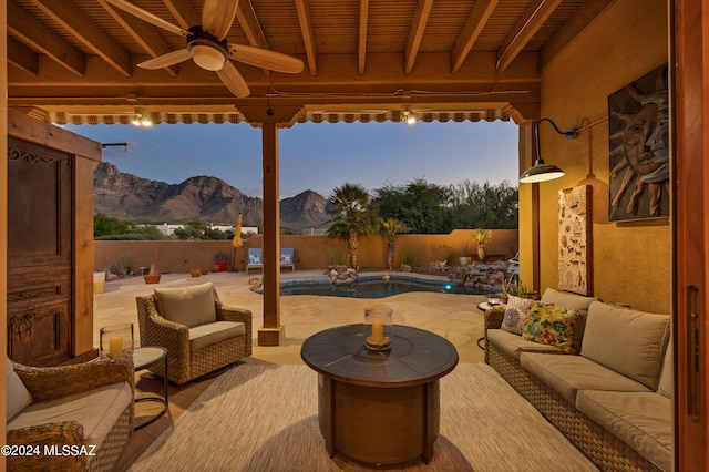 patio terrace at dusk with ceiling fan, outdoor lounge area, a mountain view, and a fenced in pool