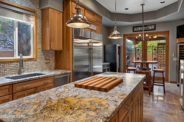 kitchen featuring tasteful backsplash, sink, hanging light fixtures, light stone countertops, and appliances with stainless steel finishes