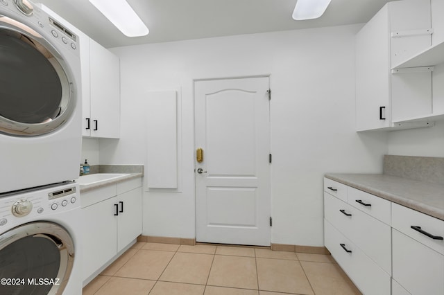 clothes washing area featuring cabinets, light tile patterned floors, stacked washer and clothes dryer, and sink