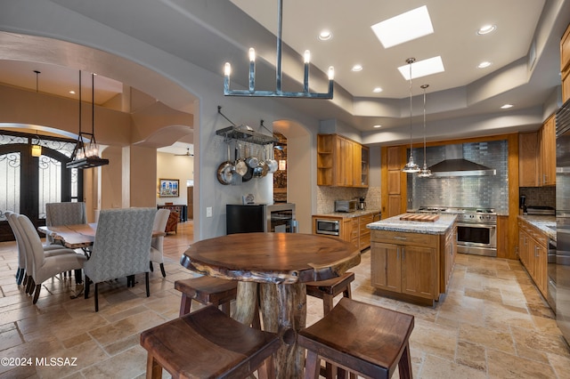 kitchen with light stone countertops, pendant lighting, appliances with stainless steel finishes, wall chimney exhaust hood, and backsplash