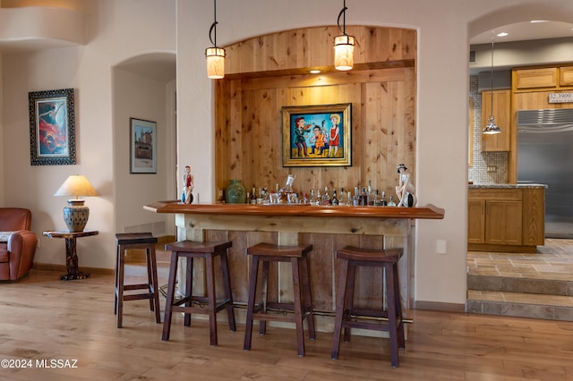 bar with light wood-type flooring, built in refrigerator, tasteful backsplash, and hanging light fixtures