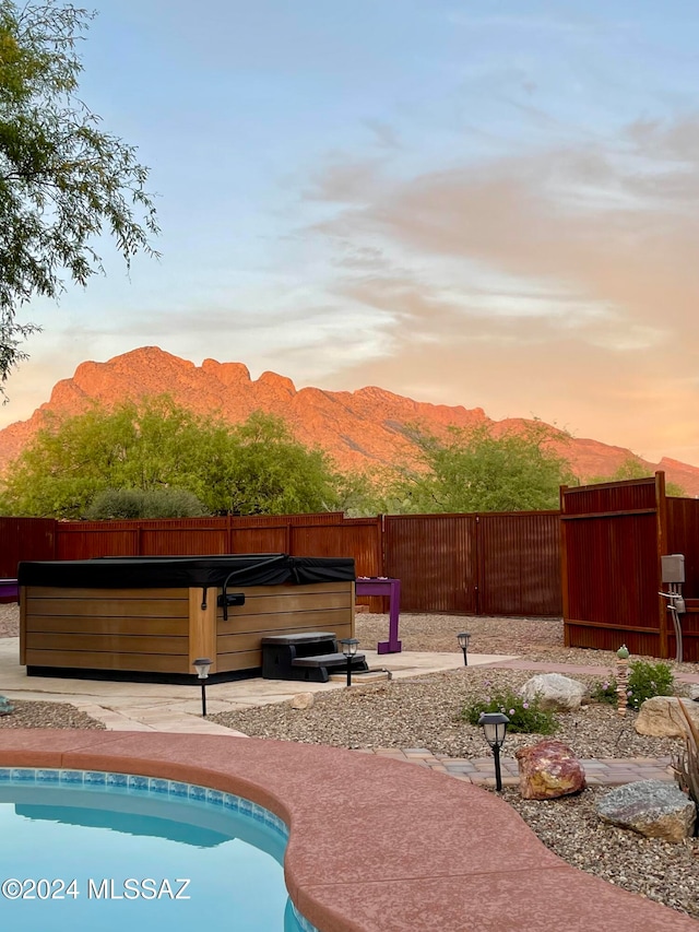 pool at dusk with a mountain view and a hot tub