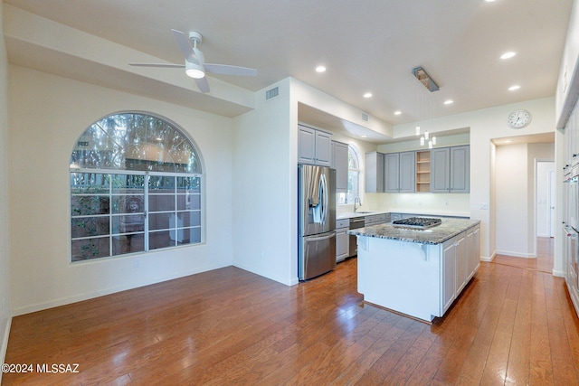 kitchen featuring hardwood / wood-style flooring, a kitchen island, open shelves, stainless steel appliances, and dark stone counters