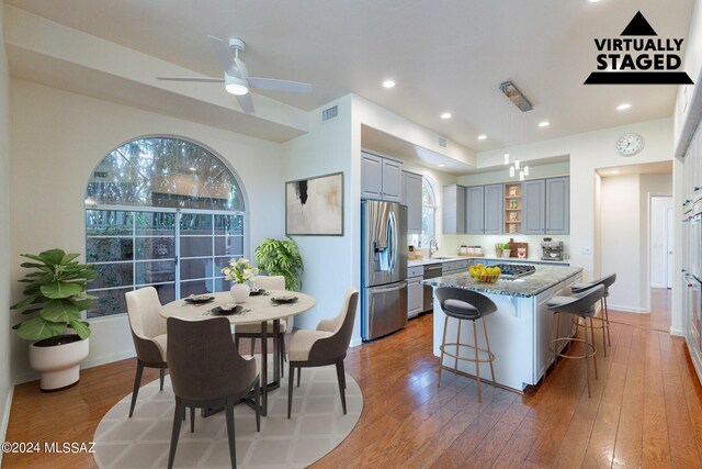 kitchen with stainless steel fridge, dark stone countertops, gray cabinets, ceiling fan, and hardwood / wood-style flooring