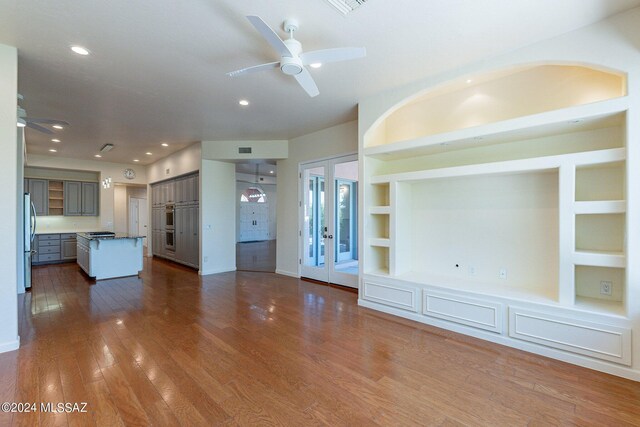 unfurnished living room with built in shelves, dark hardwood / wood-style floors, ceiling fan, and french doors