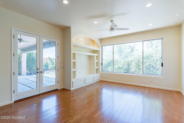 empty room featuring wood-type flooring, built in shelves, ceiling fan, and french doors