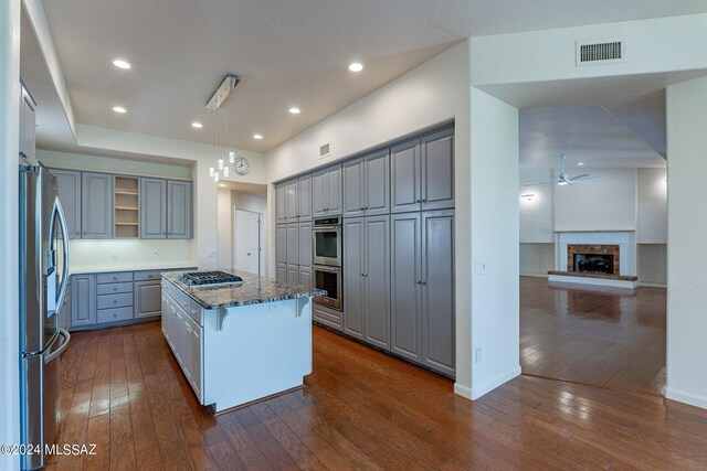 kitchen with gray cabinets, a kitchen island, a kitchen breakfast bar, appliances with stainless steel finishes, and dark hardwood / wood-style flooring