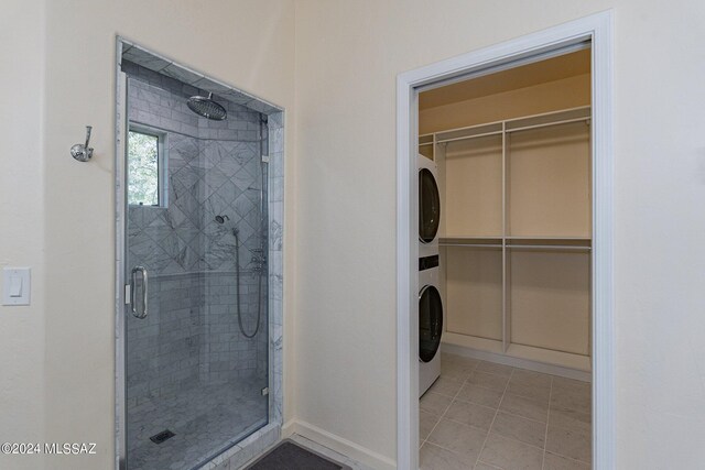 bathroom with tile patterned floors, a shower with shower door, and stacked washing maching and dryer