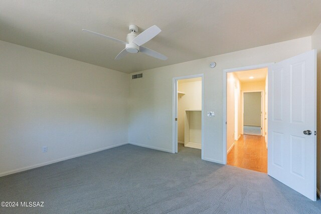 unfurnished bedroom with visible vents, carpet, baseboards, a ceiling fan, and a walk in closet