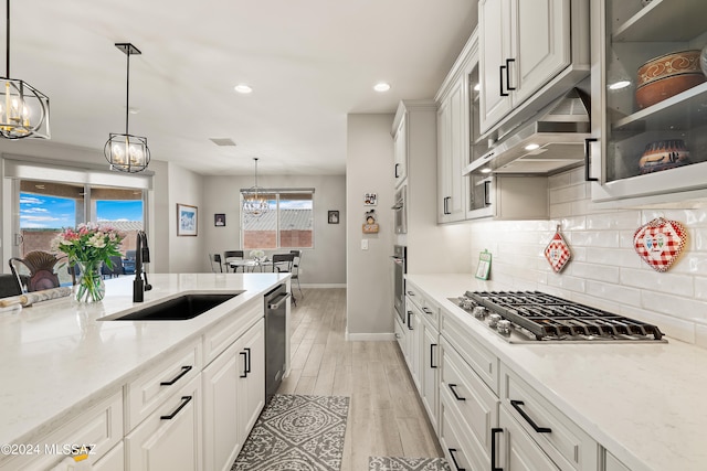 kitchen with light hardwood / wood-style floors, light stone counters, white cabinets, decorative light fixtures, and sink