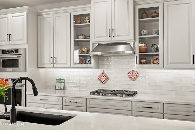 kitchen with stainless steel appliances, white cabinets, wall chimney range hood, and sink