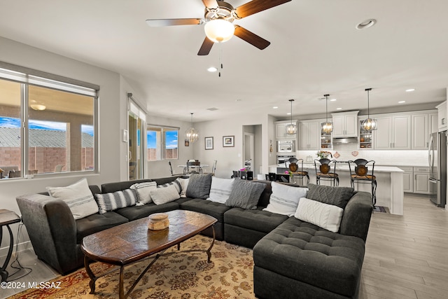 living room with ceiling fan with notable chandelier and light hardwood / wood-style floors