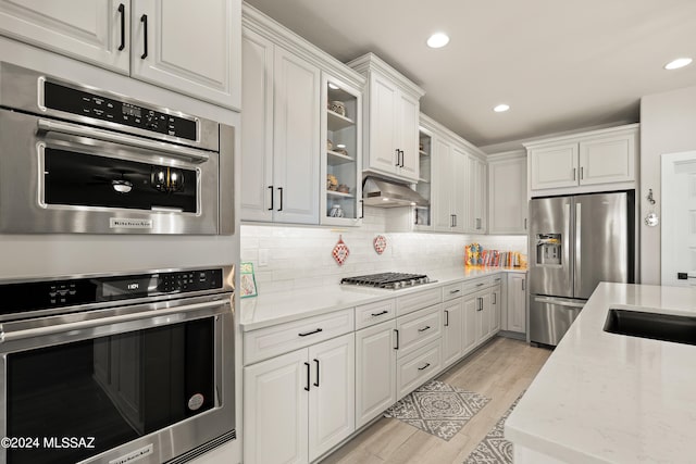 kitchen featuring tasteful backsplash, white cabinetry, light hardwood / wood-style flooring, appliances with stainless steel finishes, and light stone countertops