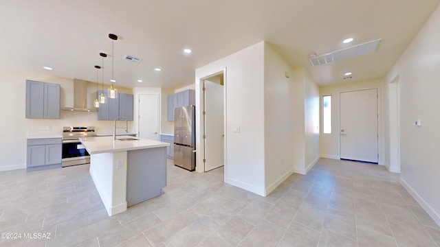 kitchen featuring gray cabinetry, wall chimney exhaust hood, stainless steel appliances, an island with sink, and pendant lighting