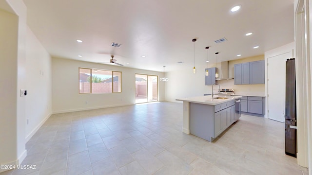 kitchen with stainless steel refrigerator, ceiling fan, gray cabinetry, an island with sink, and decorative light fixtures