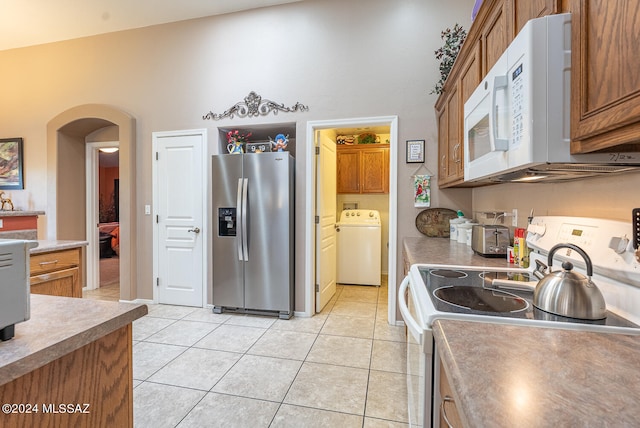 kitchen with light tile patterned flooring, lofted ceiling, stove, washer / dryer, and stainless steel fridge with ice dispenser