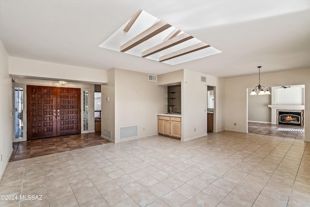 unfurnished living room featuring a notable chandelier, light tile patterned floors, and a skylight