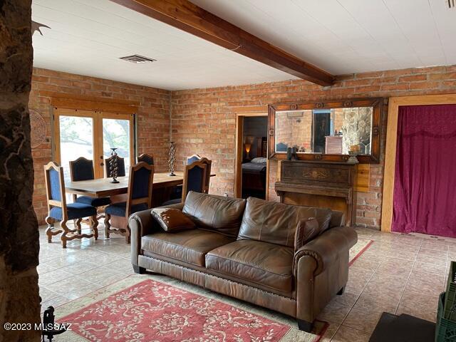 tiled living area featuring beam ceiling, visible vents, and brick wall