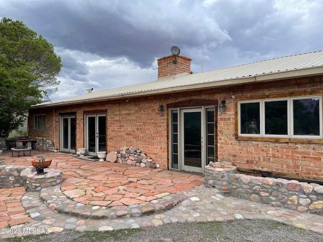 back of house with a patio, a chimney, metal roof, french doors, and brick siding