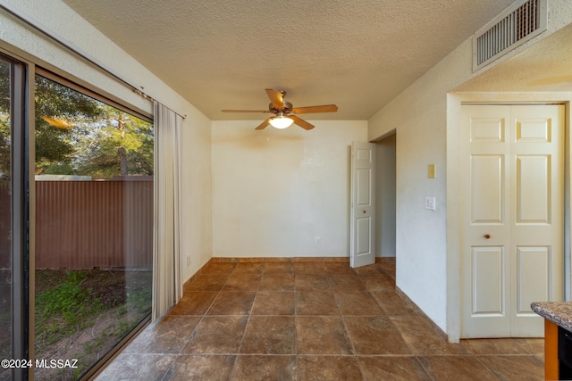 spare room with a textured ceiling, ceiling fan, and dark tile patterned flooring