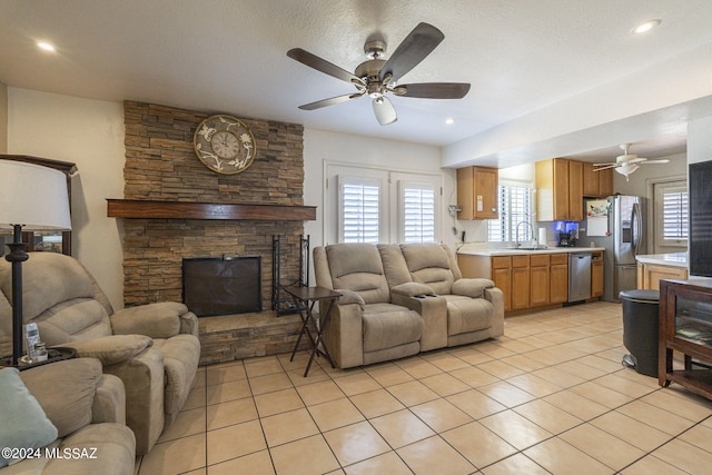 living room with a stone fireplace, light tile patterned floors, a textured ceiling, ceiling fan, and sink