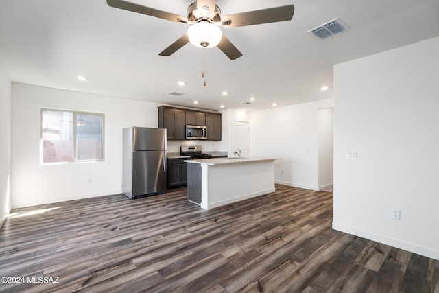 kitchen featuring ceiling fan, dark brown cabinetry, a center island with sink, appliances with stainless steel finishes, and dark hardwood / wood-style flooring