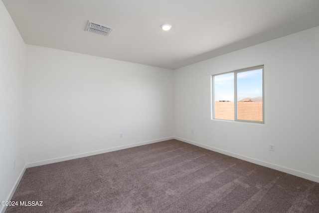 empty room with dark carpet, visible vents, and baseboards