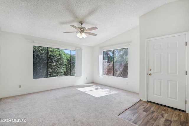 carpeted empty room with a textured ceiling, vaulted ceiling, and ceiling fan