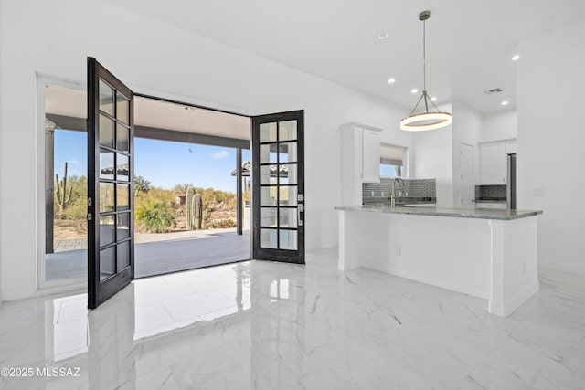 kitchen with french doors, white cabinetry, decorative light fixtures, kitchen peninsula, and light stone countertops