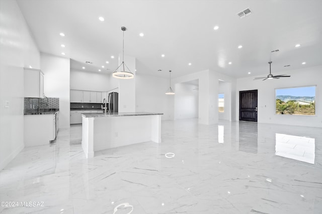 kitchen with stainless steel fridge, white cabinets, decorative backsplash, hanging light fixtures, and a kitchen island with sink