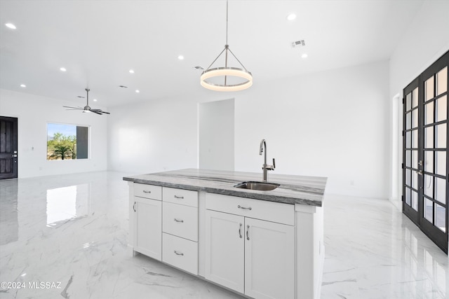 kitchen featuring sink, white cabinetry, stone countertops, hanging light fixtures, and a kitchen island with sink